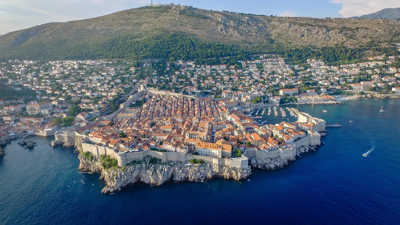 Luchtfoto van de ommuurde oude stad van Dubrovnik op de rotsen aan zee, met de berg Srđ op de achtergrond