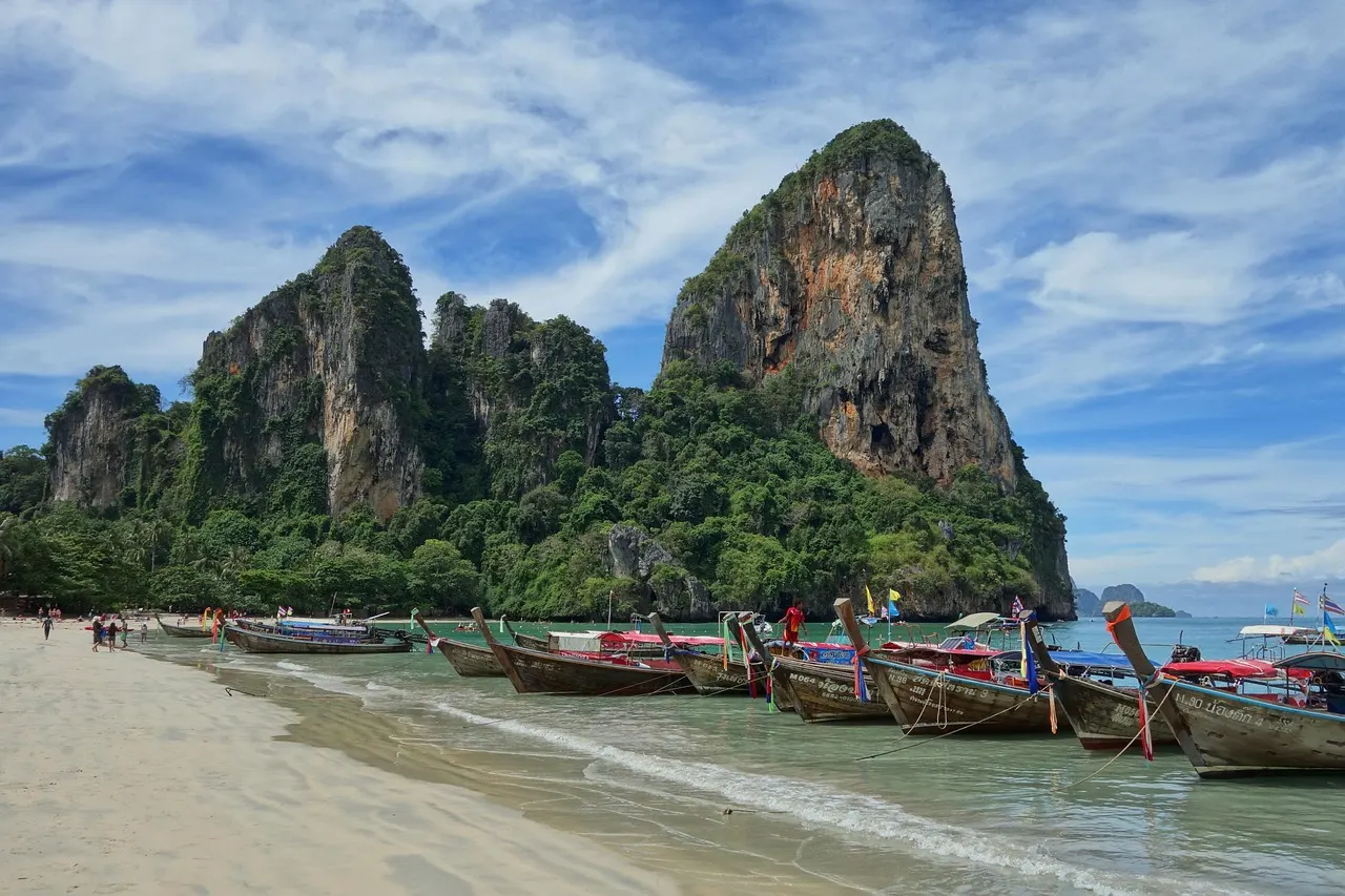 Longtailboten op het strand van Railay Beach met hoge kalksteenrotsen en groene begroeiing op de achtergrond