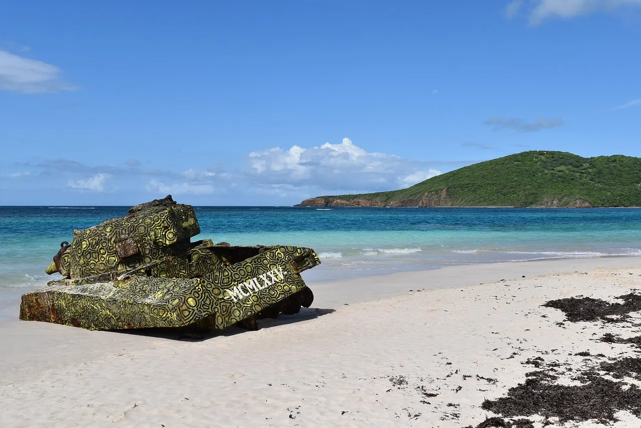 Beschilderde oude tank op het witte strand van Playa Flamenco met turquoise zee en groene heuvel