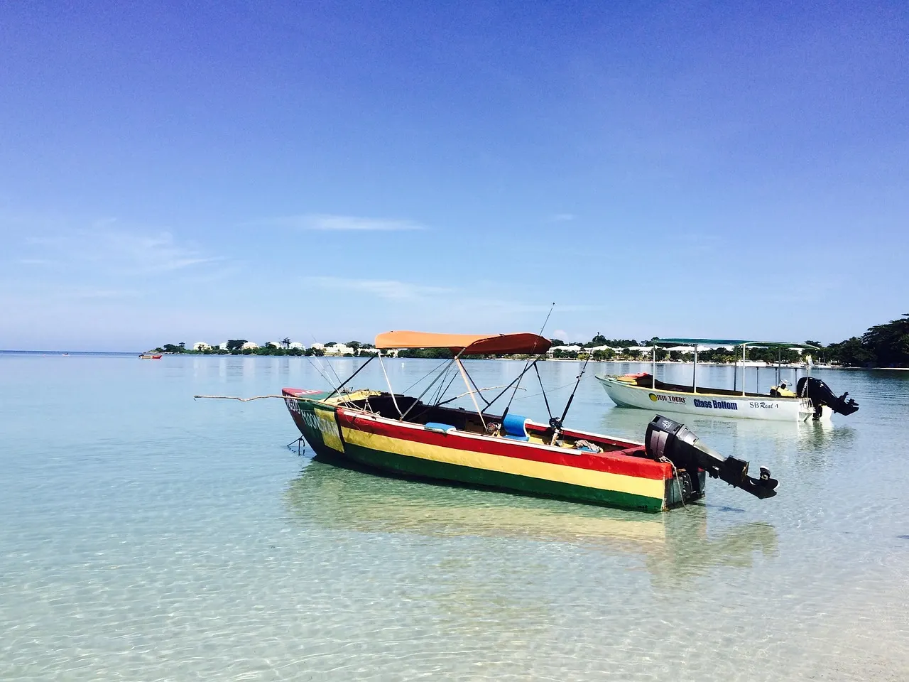 Boot in Jamaicaanse kleuren op helder turquoise water bij het strand van Negril onder een blauwe lucht