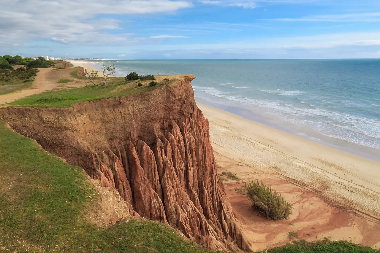 Rode, geërodeerde klif boven het lange zandstrand van Praia da Falésia aan zee