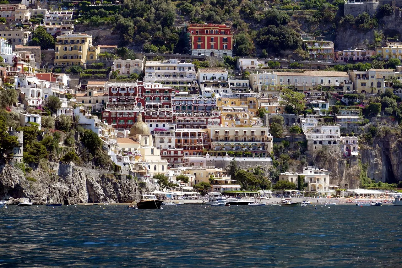 Kleurrijke huizen van Positano tegen de rotsige heuvel, gezien vanaf de zee met bootjes bij het strand