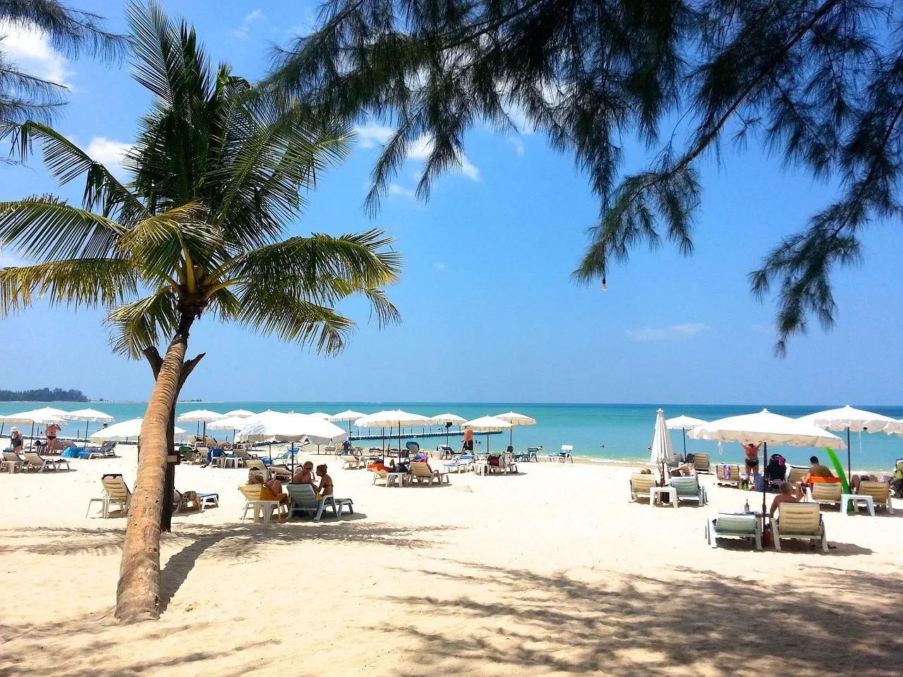 Zandstrand van Khao Lak met palmboom, witte parasols en ligbedden aan een helderblauwe zee