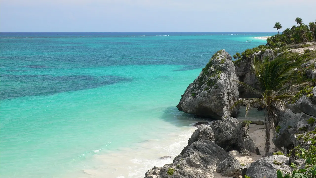 Turquoise zee en wit zandstrand tussen grijze rotsen en palmbomen aan de kust van Tulum