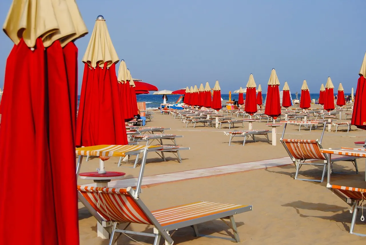 Rijen rode parasols en strandstoelen op het zandstrand van Rimini met de blauwe zee op de achtergrond