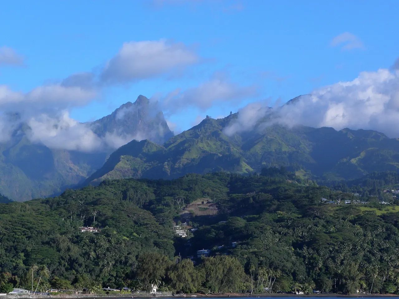 Groene bergtoppen van Tahiti met wolken boven de beboste kust aan de lagune