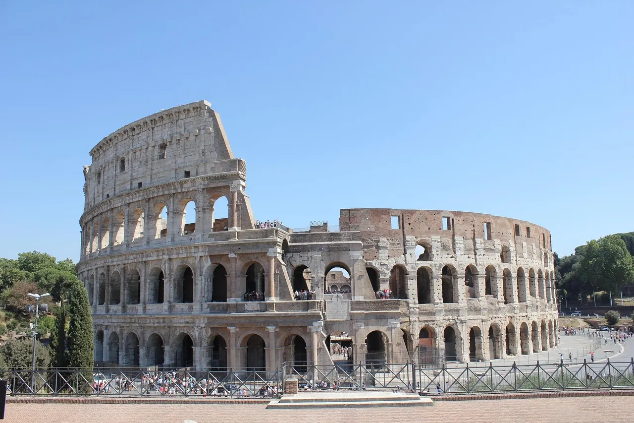 Het Colosseum in Rome van buiten onder een strakblauwe lucht, met de hoge en ingestorte buitenmuur