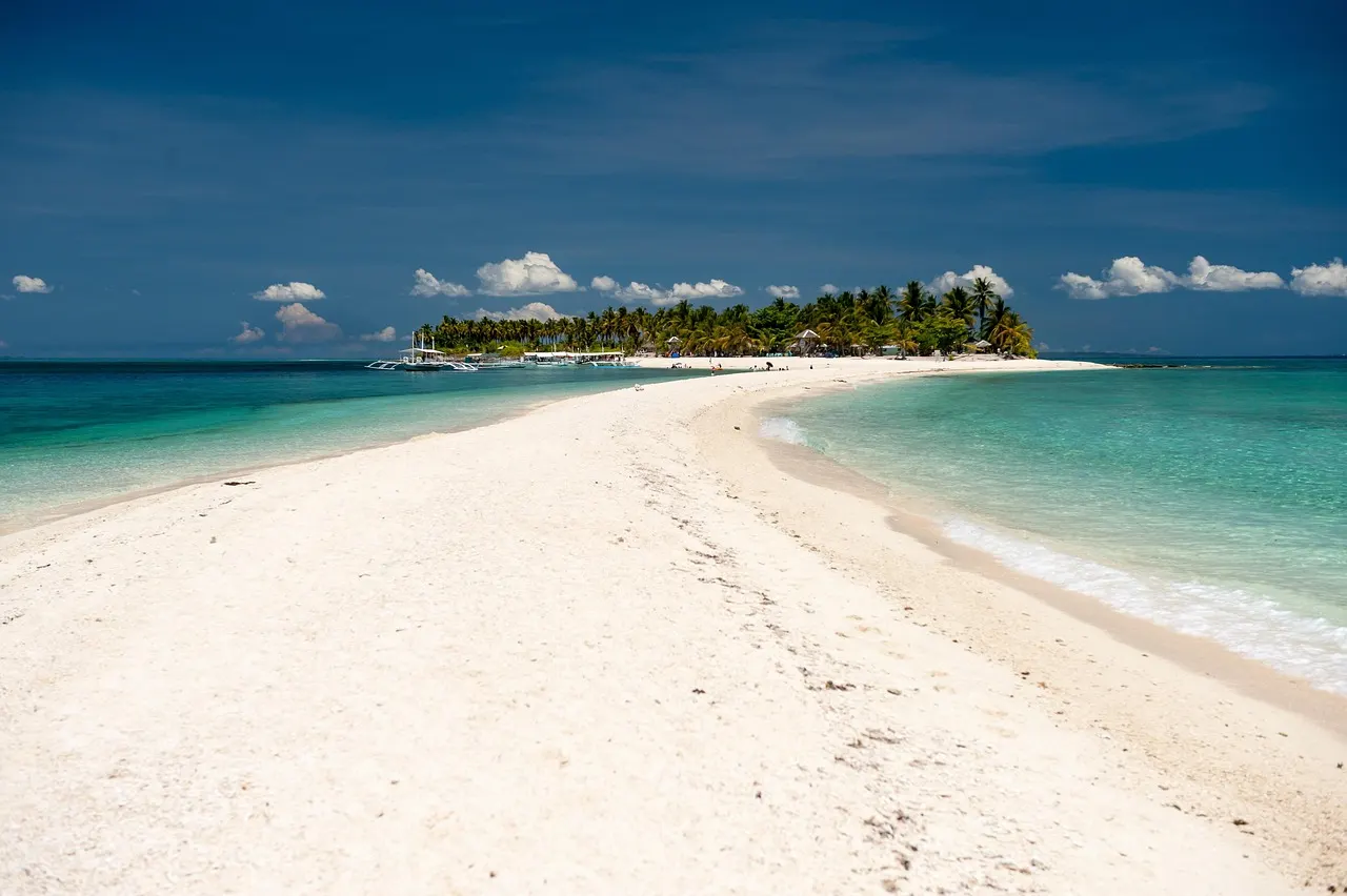 Lange witte zandbank van Kalanggaman Island met turquoise water aan beide kanten en palmbomen op de achtergrond