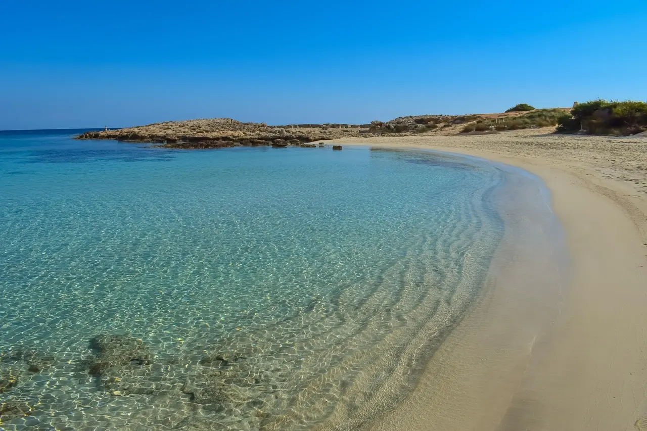 Zandstrand met helder turquoise water en rotsachtige landtong onder een strakblauwe lucht bij Ayia Napa