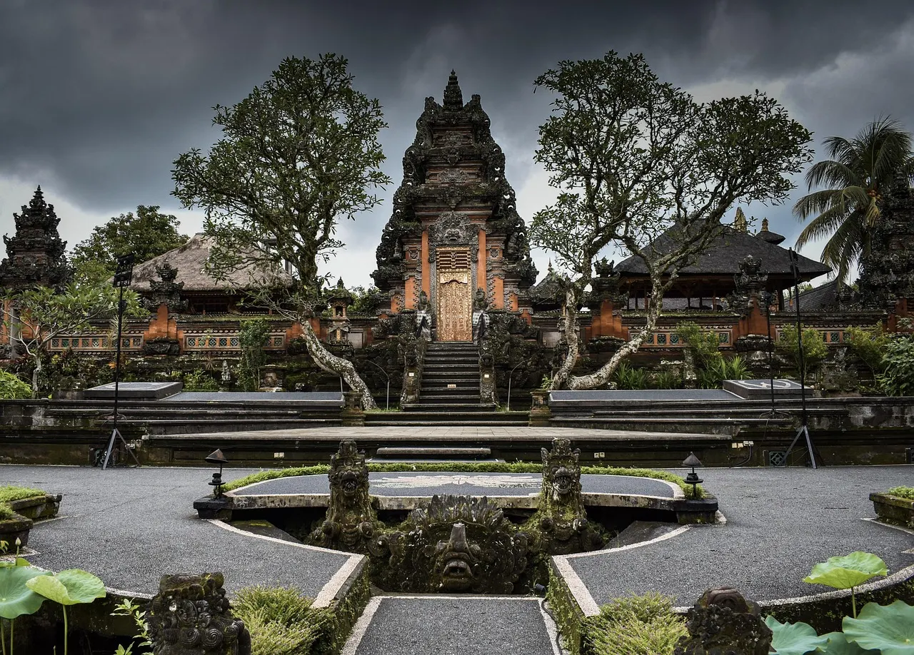 Pura Taman Saraswati in Ubud met rijk versierde tempelpoort, stenen beelden en lotusvijvers onder een donkere lucht