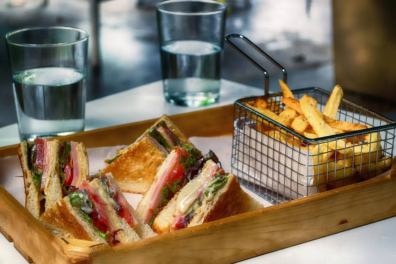 Clubsandwiches op een houten dienblad met een mandje frietjes en glazen water