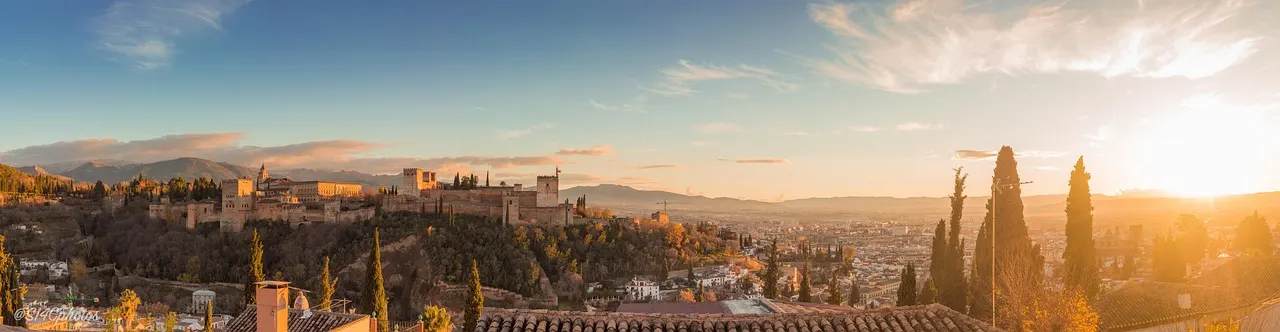 Panorama van het Alhambra op de heuvel boven Granada bij zonsondergang, met bergen op de achtergrond