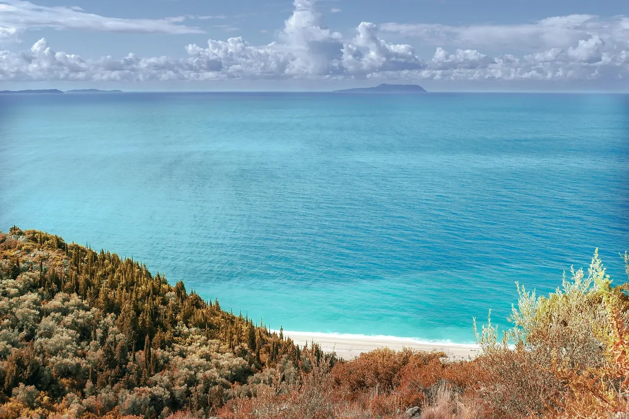 Turquoise zee en wit strand onder een groene heuvelflank aan de Albanese Rivièra