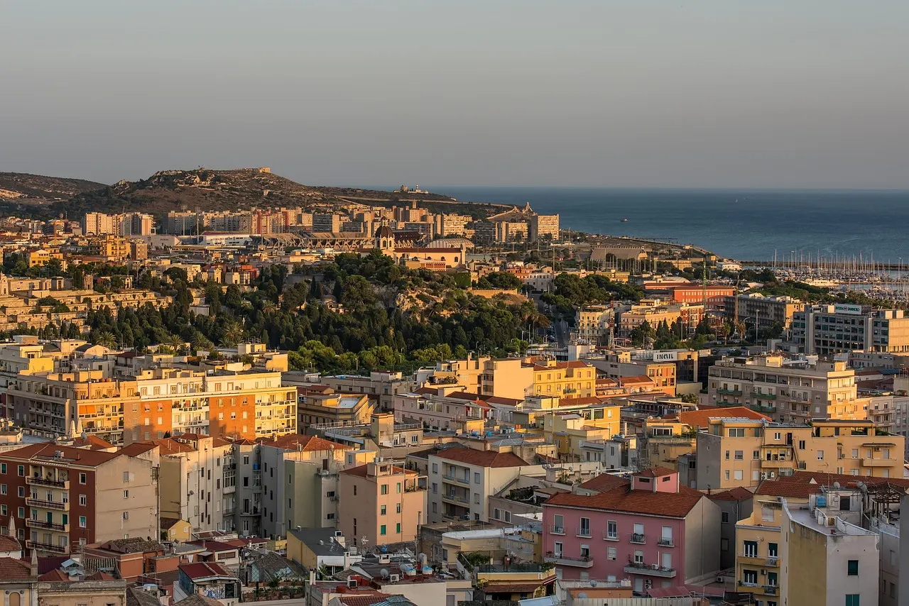 Uitzicht over de daken van Cagliari met groene heuvels en de zee in warm avondlicht