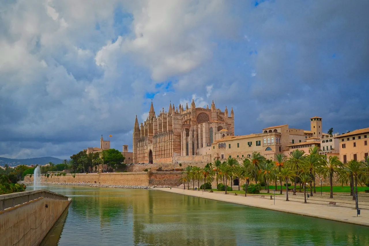 Kathedraal La Seu van Palma met palmbomen en het waterbassin van Parc de la Mar onder een bewolkte lucht