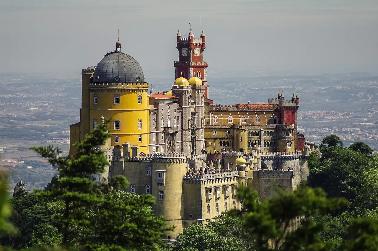 Het kleurrijke Pena-paleis met gele koepel en rode klokkentoren op een beboste heuvel bij Sintra