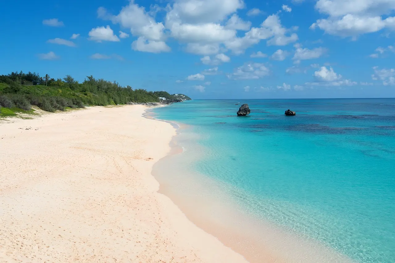 Lichtroze zandstrand langs turquoise zee met rotsen in het water en groene begroeiing op Bermuda