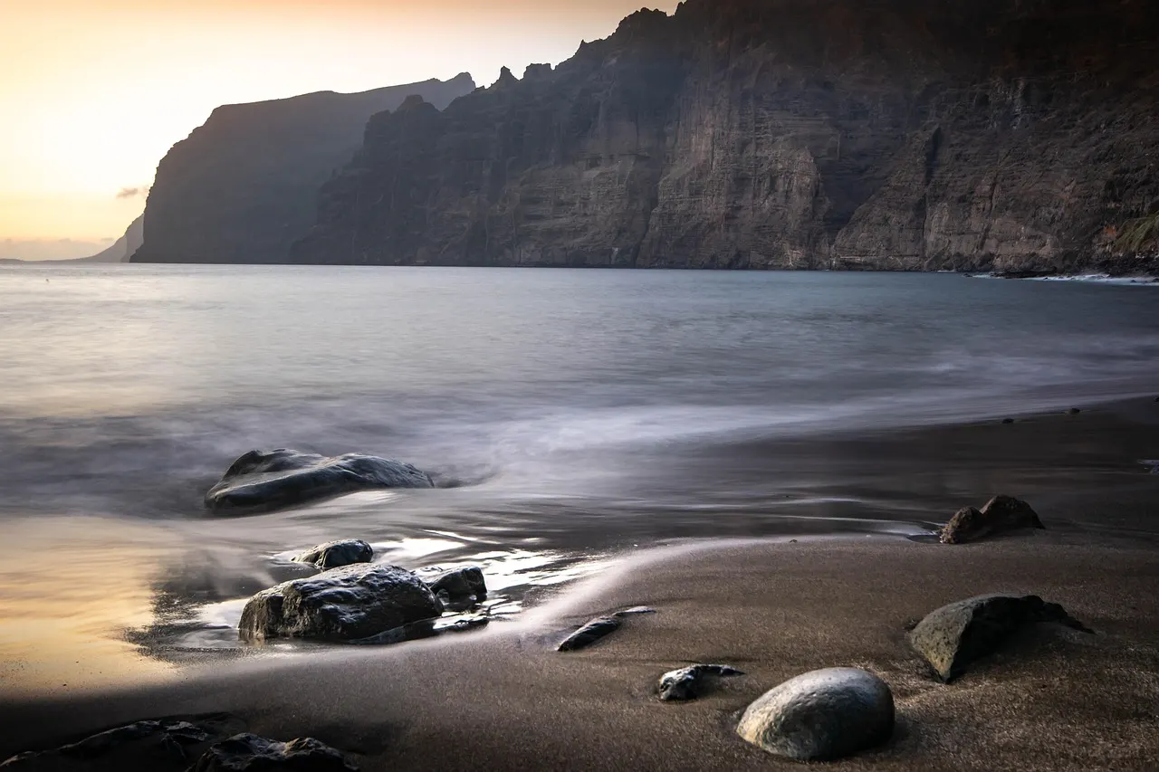 Zwart lavastrand met ronde stenen voor de steile kliffen van Los Gigantes op Tenerife bij zonsondergang