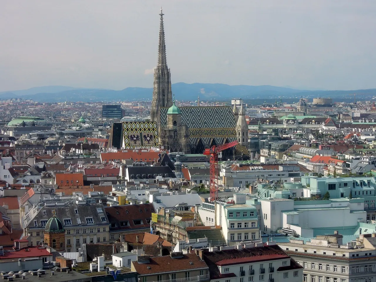 Uitzicht over de daken van Wenen met de Stephansdom en zijn kleurrijke pannendak, bergen op de achtergrond