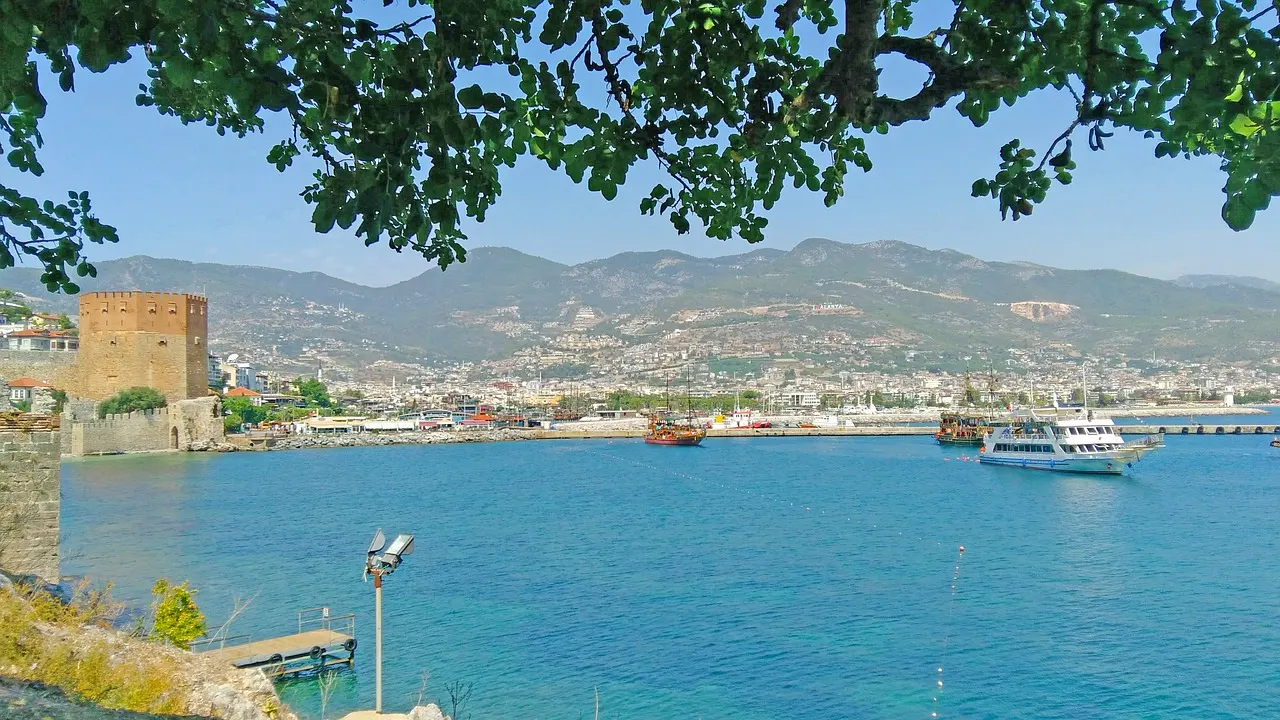 Uitzicht over de haven van Alanya met de Rode Toren, boten en de stad tegen de bergen