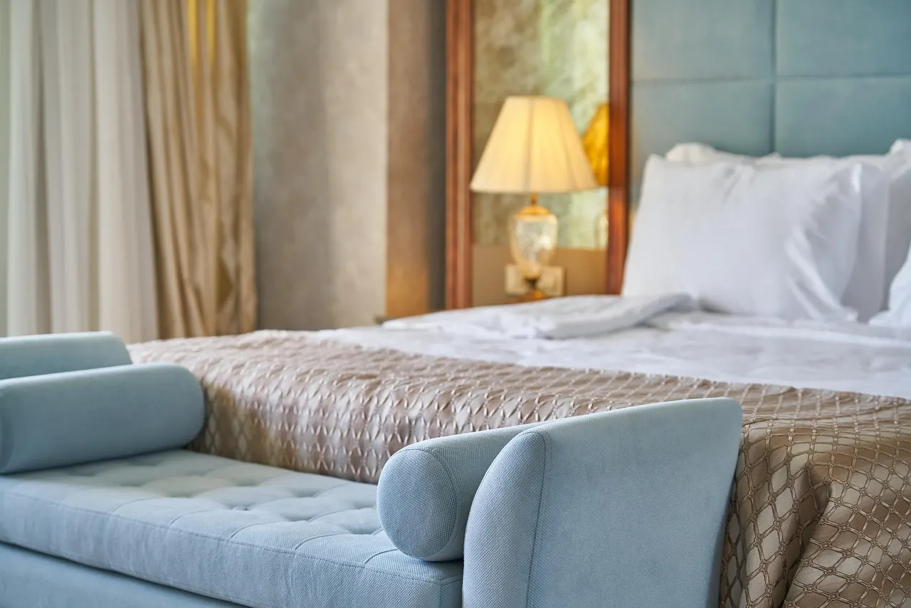 Luxe hotelsuite met lichtblauwe gecapitonneerde bank aan het voeteneinde van een opgemaakt bed