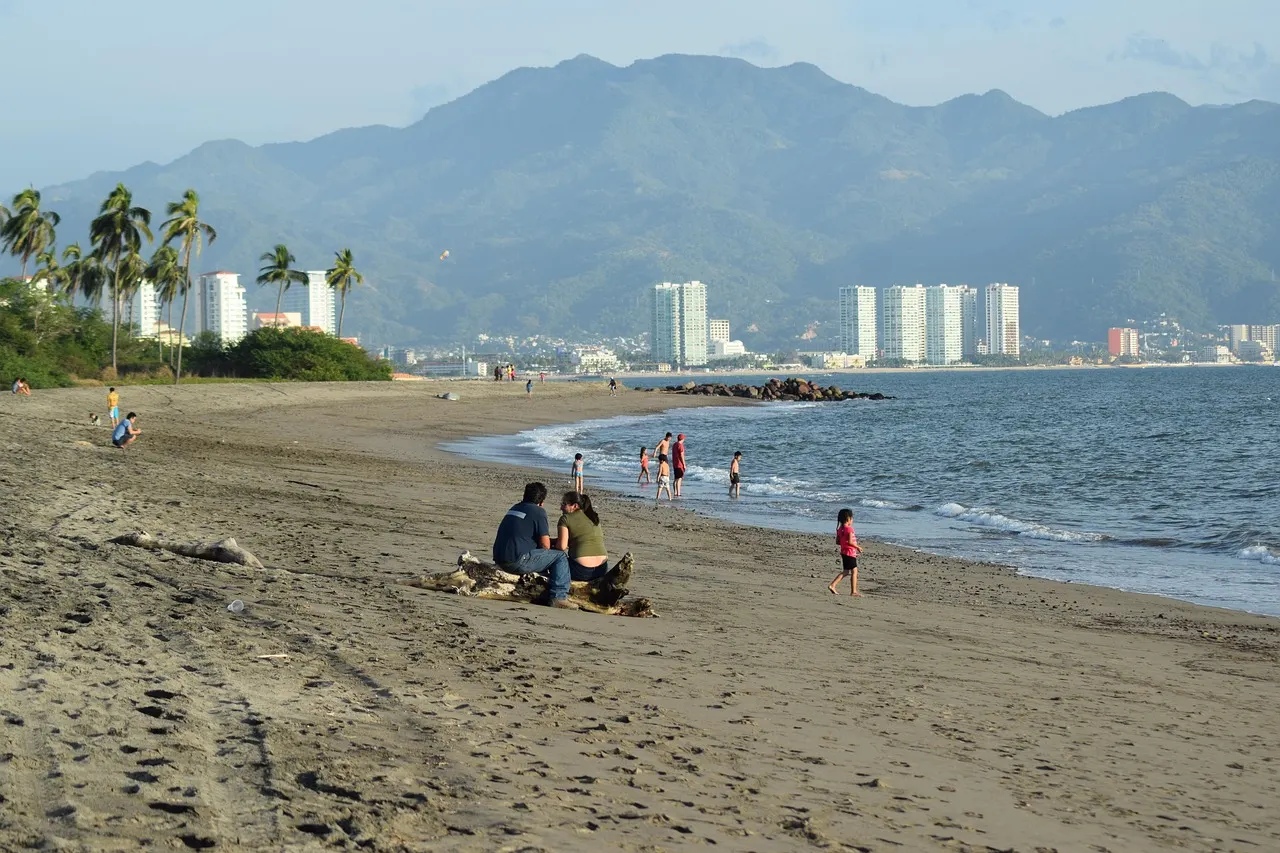 Zandstrand aan de baai van Puerto Vallarta met hoge flatgebouwen en groene bergen op de achtergrond