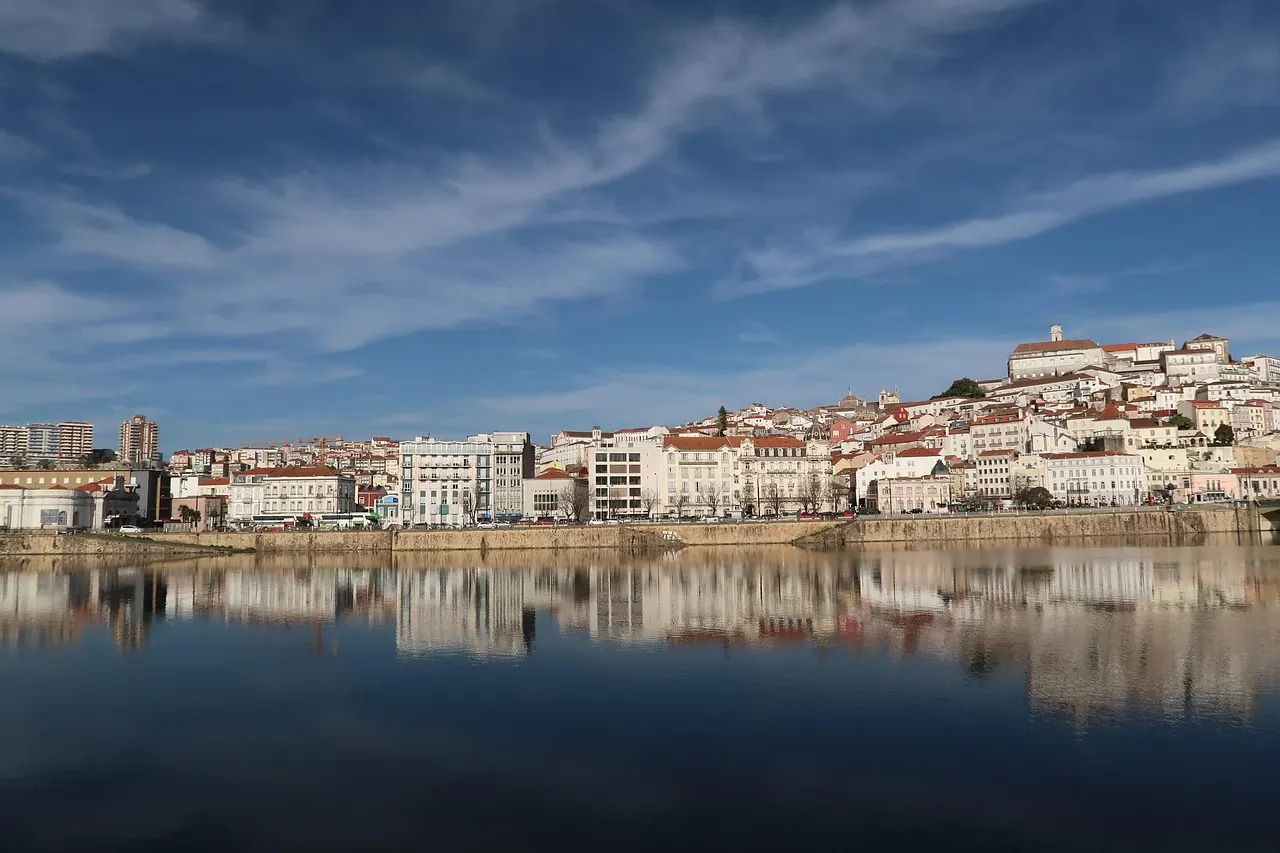 Oude stad van Coimbra op de heuvel met de universiteit, weerspiegeld in de rivier de Mondego onder een blauwe lucht