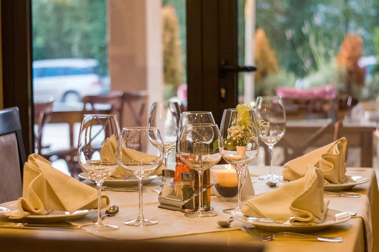 Gedekte restauranttafel met wijnglazen, gevouwen servetten en een kaarsje bij het raam