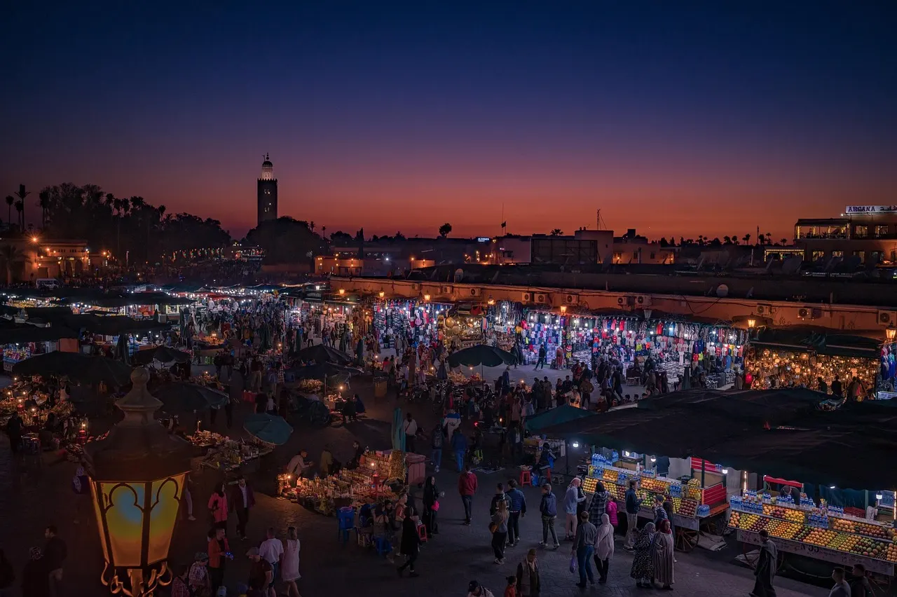 Djemaa el-Fna-plein in Marrakech bij schemering met verlichte marktkraampjes en de Koutoubia-minaret
