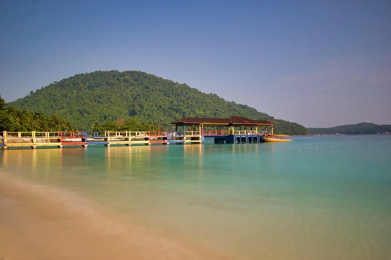 Turquoise water en zandstrand met een steiger en paviljoen voor een beboste heuvel op de Perhentian-eilanden