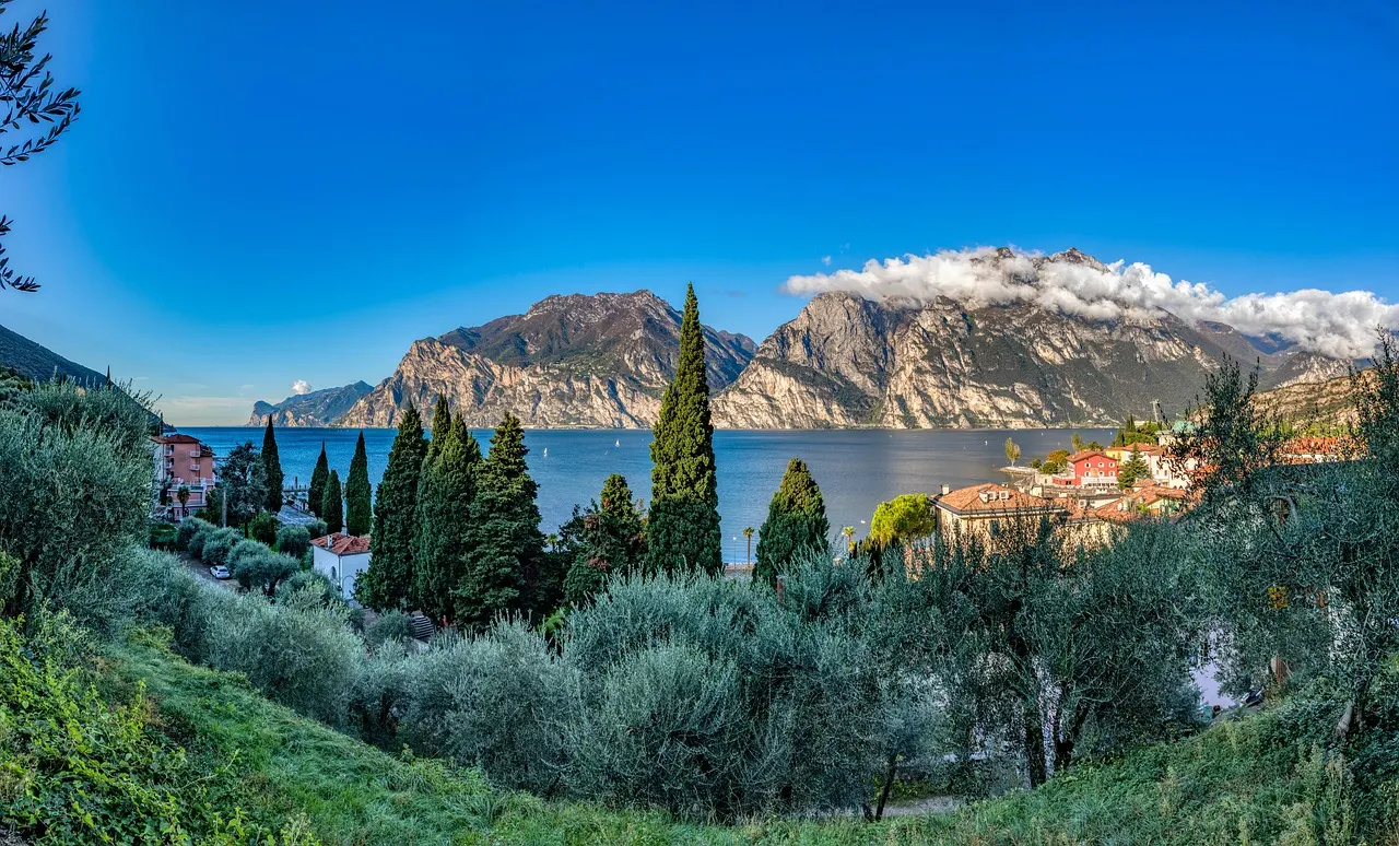 Panoramisch uitzicht over het blauwe Gardameer met rotsachtige bergen, cipressen en olijfbomen bij Torbole
