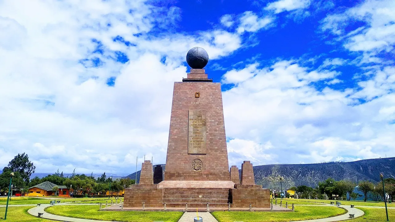 Het Mitad del Mundo-monument met de wereldbol op de top, omringd door gazons onder een blauwe lucht