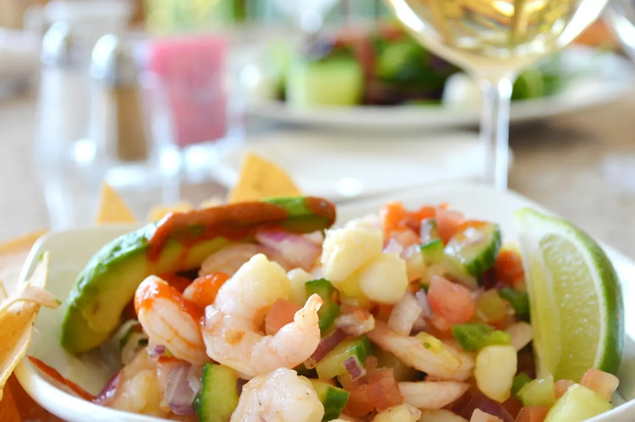 Garnalenceviche met avocado, tomaat, ui en limoen, met tortillachips en een glas witte wijn