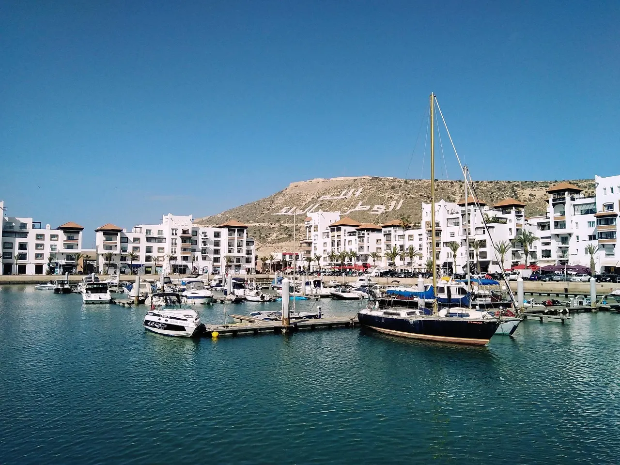 Jachthaven van Agadir met witte gebouwen en de heuvel met de Kasbah-inscriptie op de achtergrond