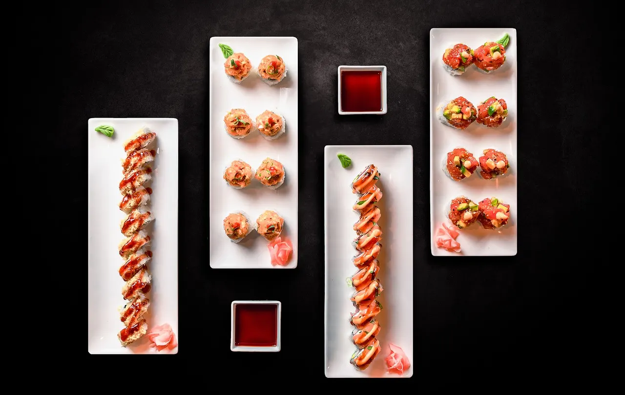 Verschillende sushirolletjes op witte borden met sojasaus op een donkere ondergrond
