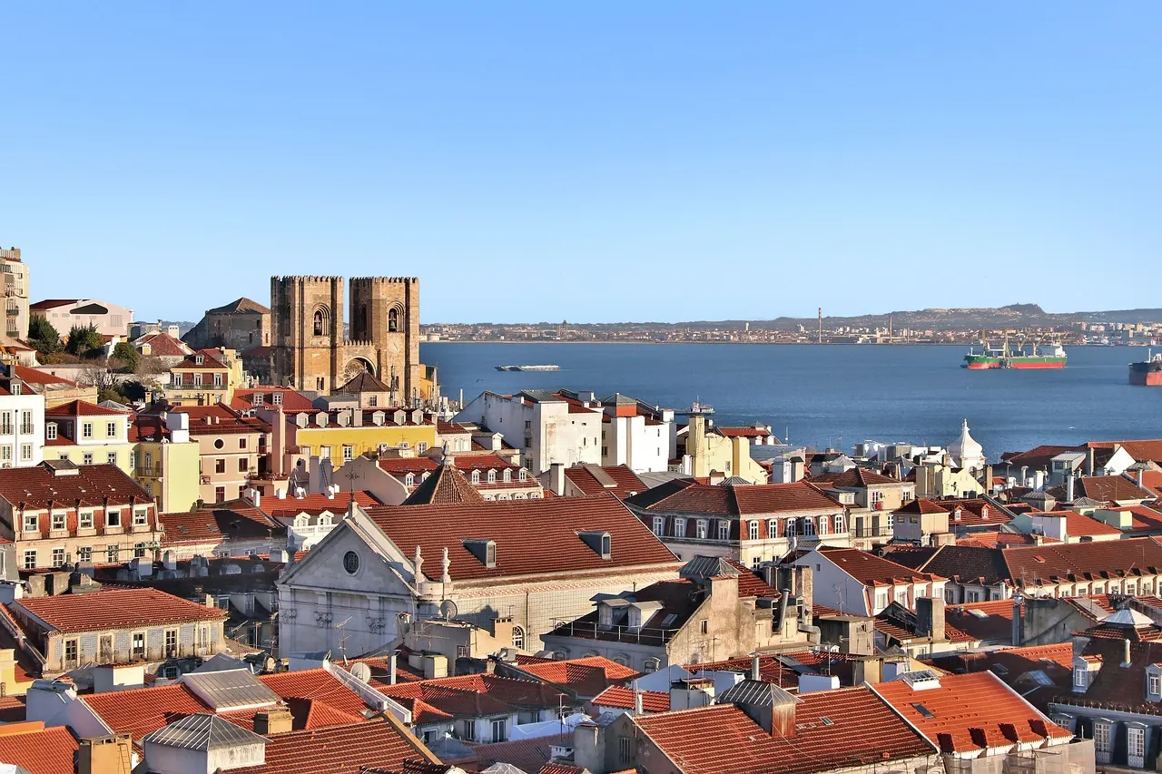 Rode daken van Lissabon met de kathedraal Sé en de Taag op de achtergrond onder een blauwe lucht