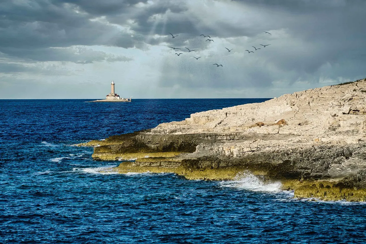 Rotsachtige kust van Kamenjak met golven en de vuurtoren Porer op zee onder een dramatische lucht