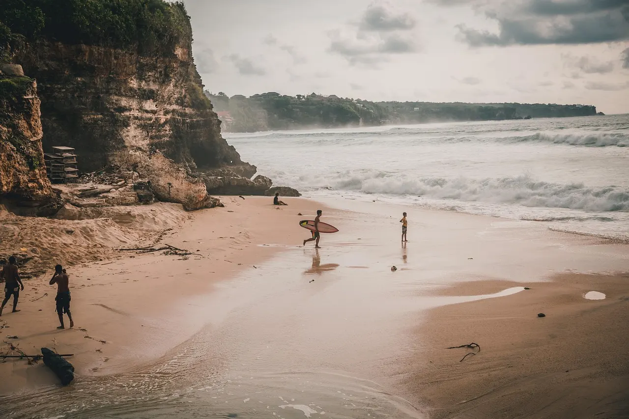 Surfers met surfplank op een zandstrand onder hoge kalkstenen kliffen bij Uluwatu, Bali