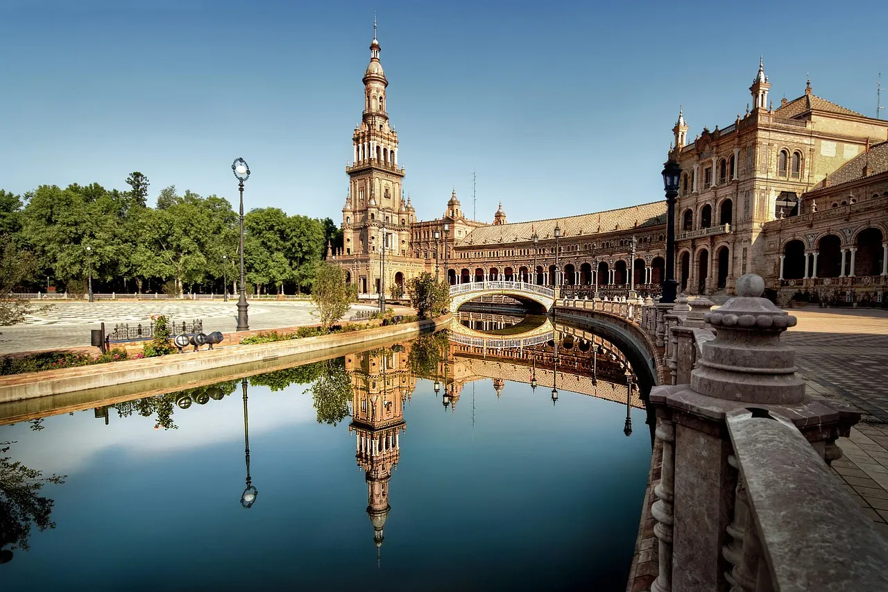 Toren en brug van Plaza de España in Sevilla, weerspiegeld in het kanaal onder een strakblauwe lucht