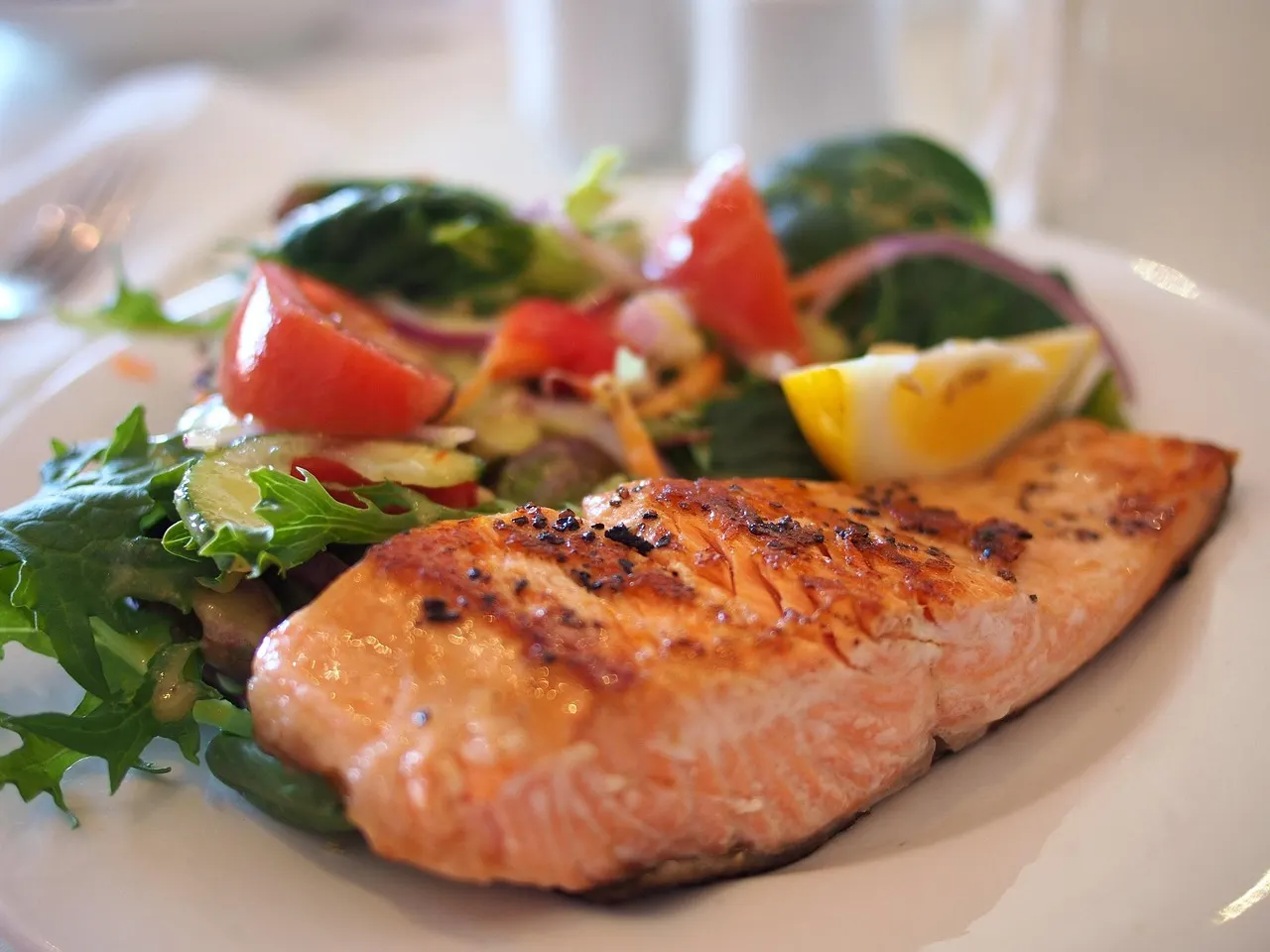Gegrilde zalmfilet met verse salade, tomaat en een partje citroen op een wit bord