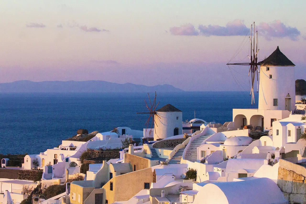 Witte huisjes en windmolens van Oia op Santorini boven de Egeïsche Zee bij zonsondergang