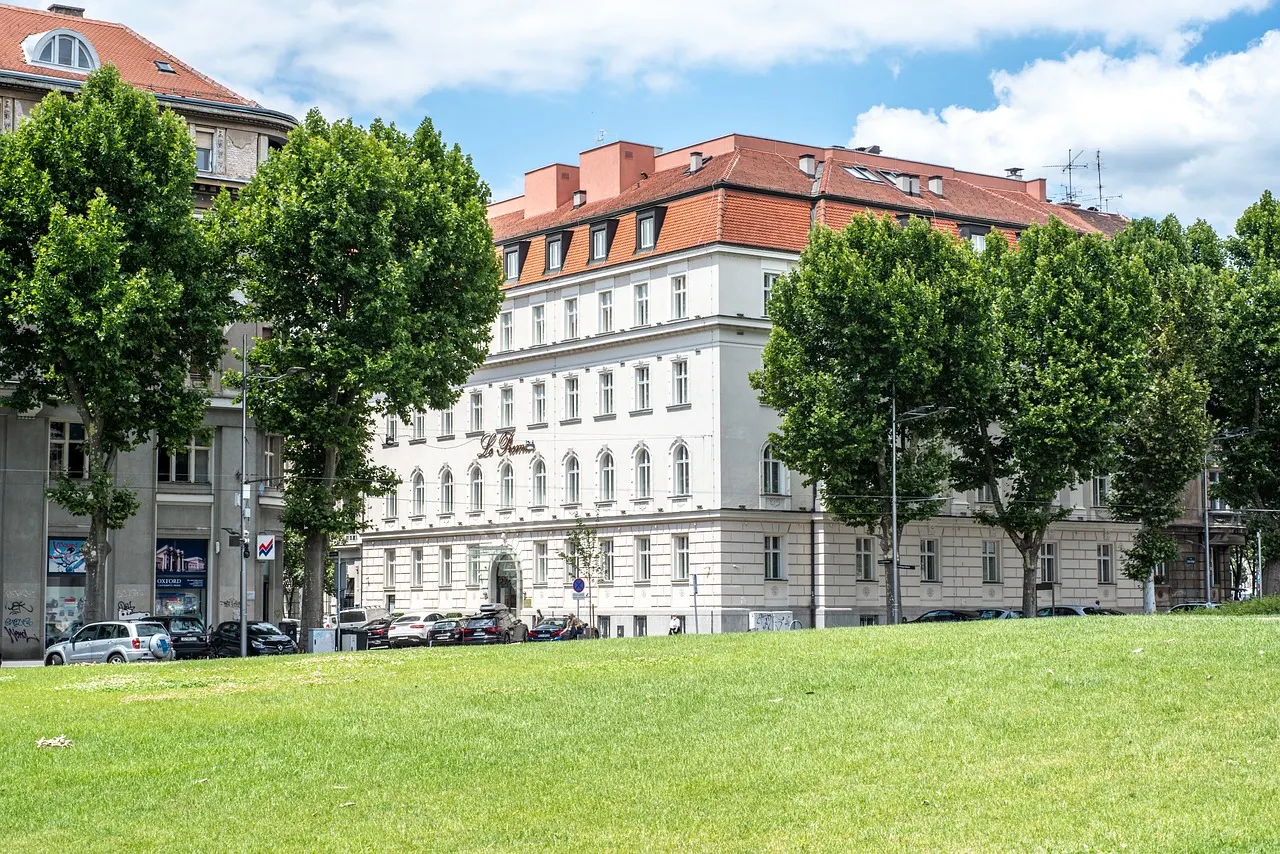 Wit hotelgebouw met rood dak achter bomen en een grasveld in Zagreb, onder een blauwe lucht