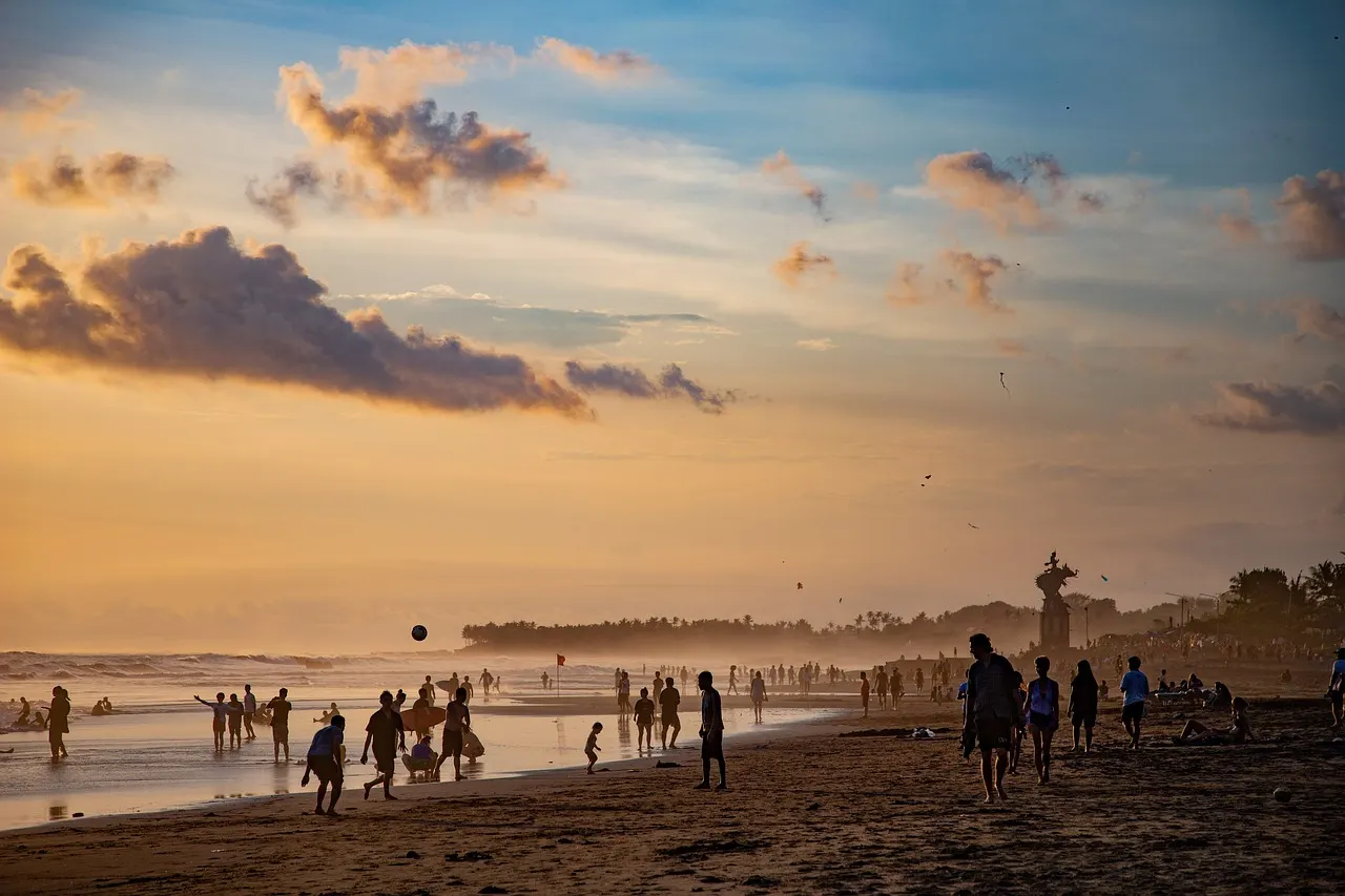Druk strand van Canggu bij zonsondergang met strandgangers, golven en een standbeeld in de verte