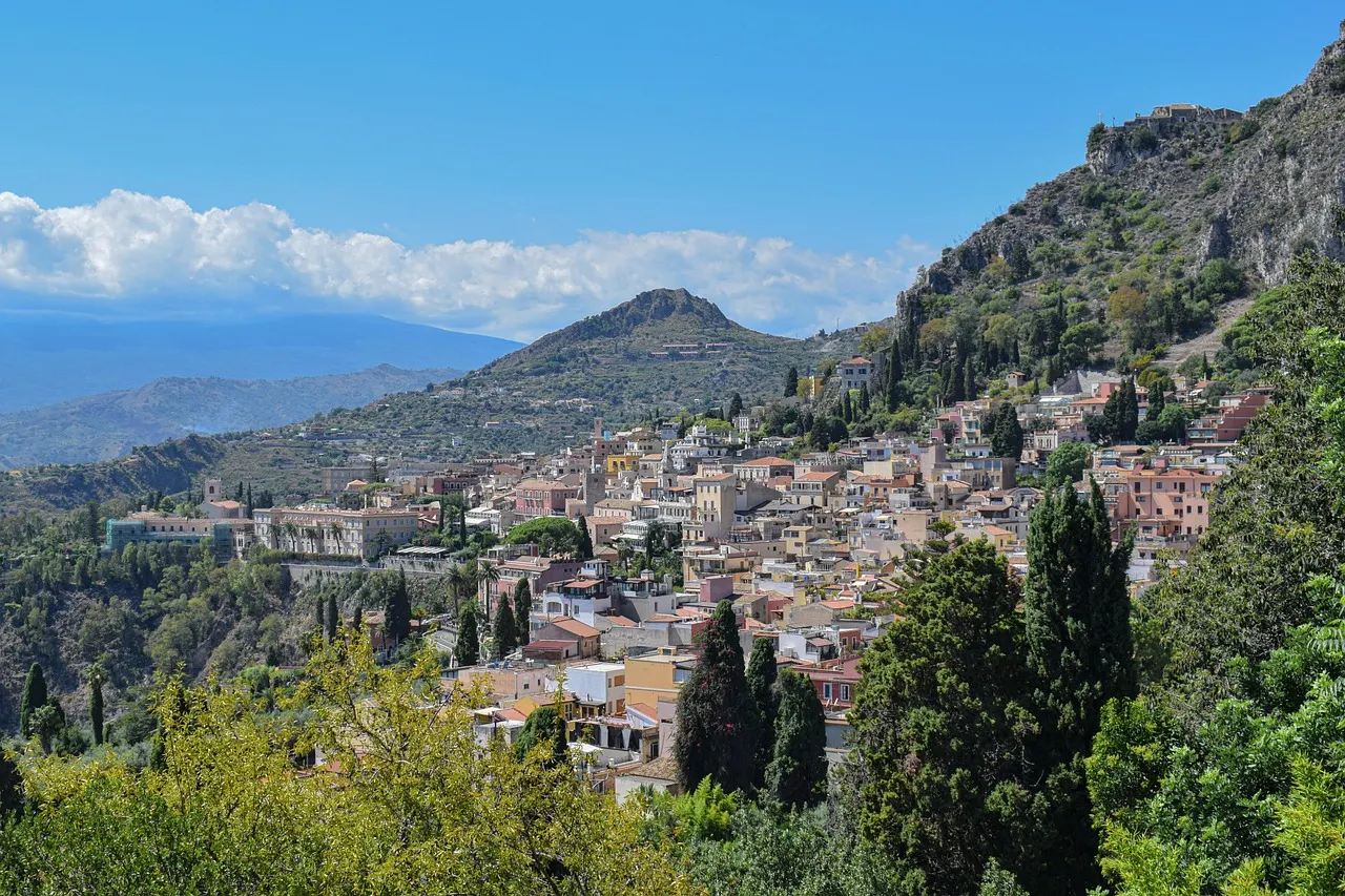 Taormina met pastelkleurige huizen tegen een groene heuvel onder een blauwe lucht op Sicilië