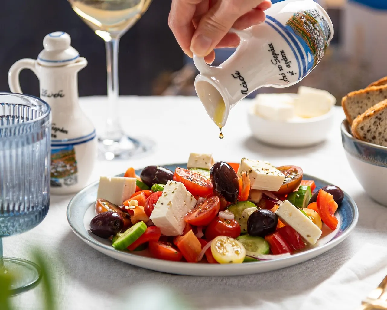 Griekse salade met feta, tomaat, komkommer en olijven waarover olijfolie wordt geschonken