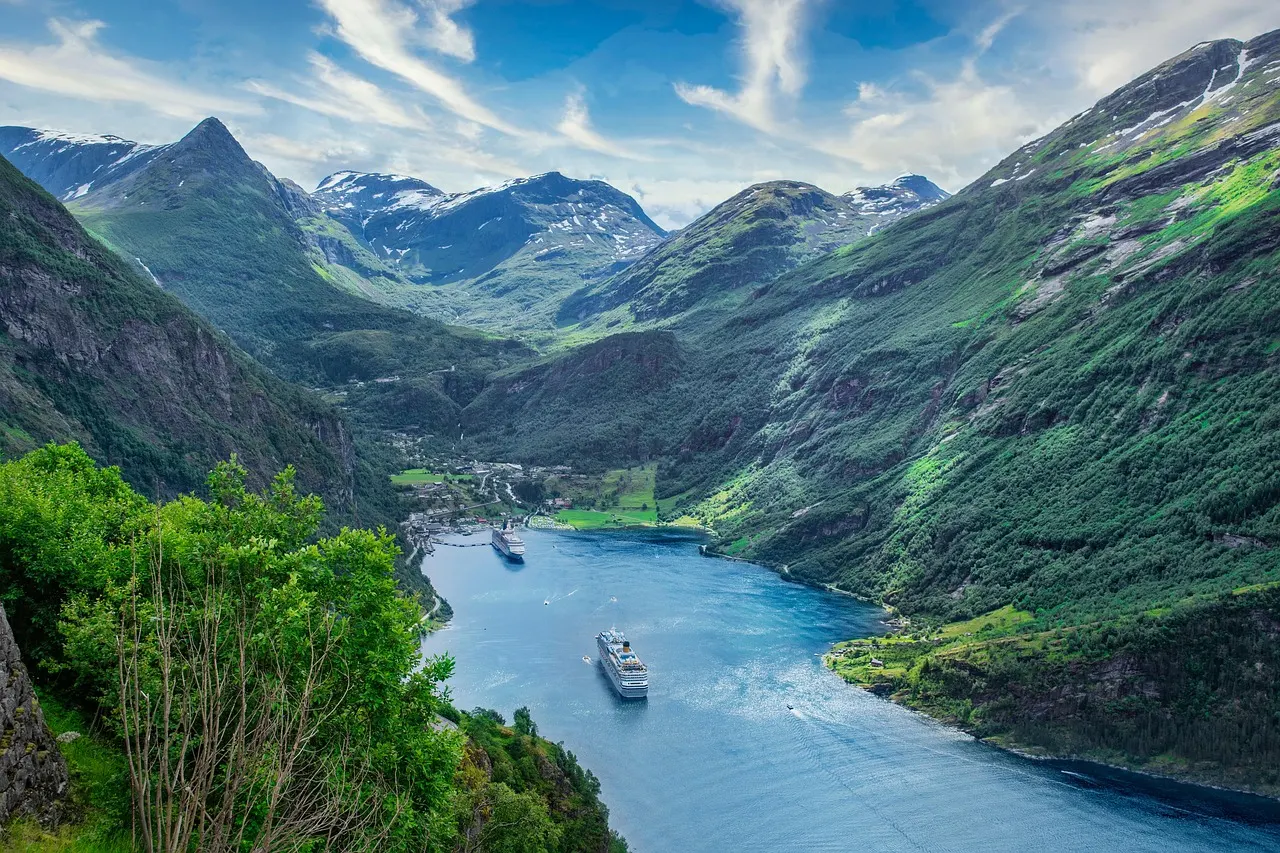 Diepblauwe fjord tussen groene bergen met besneeuwde toppen en cruiseschepen bij een dorp