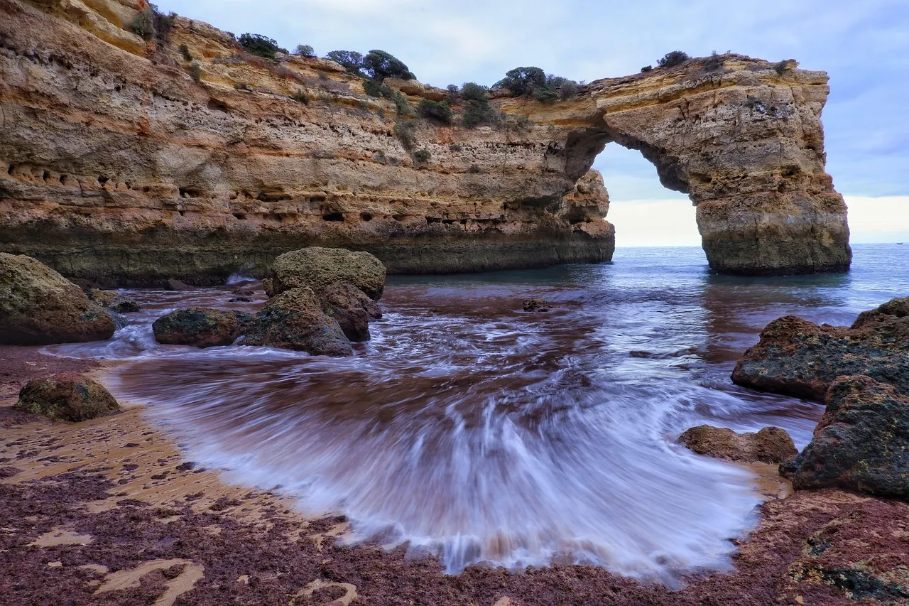 Natuurlijke rotsboog in zee bij Praia de Albandeira met golven die over het rotsige strand spoelen