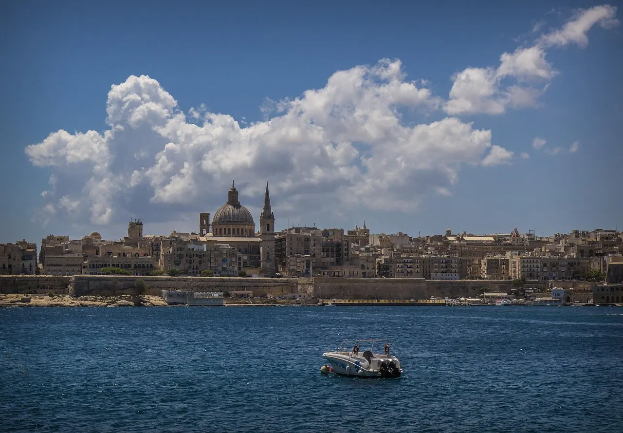 Skyline van Valletta met de koepel van de Karmelietenkerk en spits, gezien over het blauwe water met een bootje