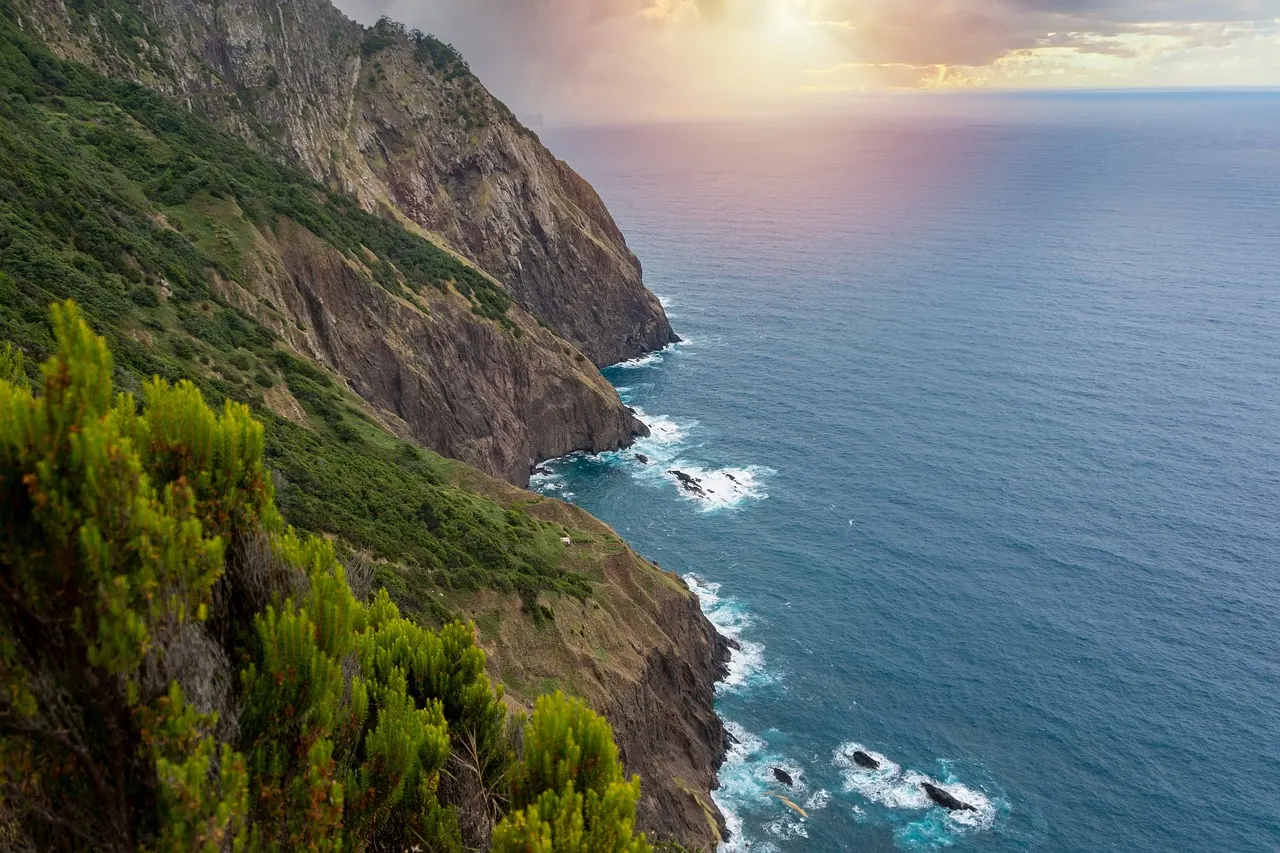 Groene, steile kliffen langs de blauwe oceaan aan de kust van Madeira bij zonsondergang