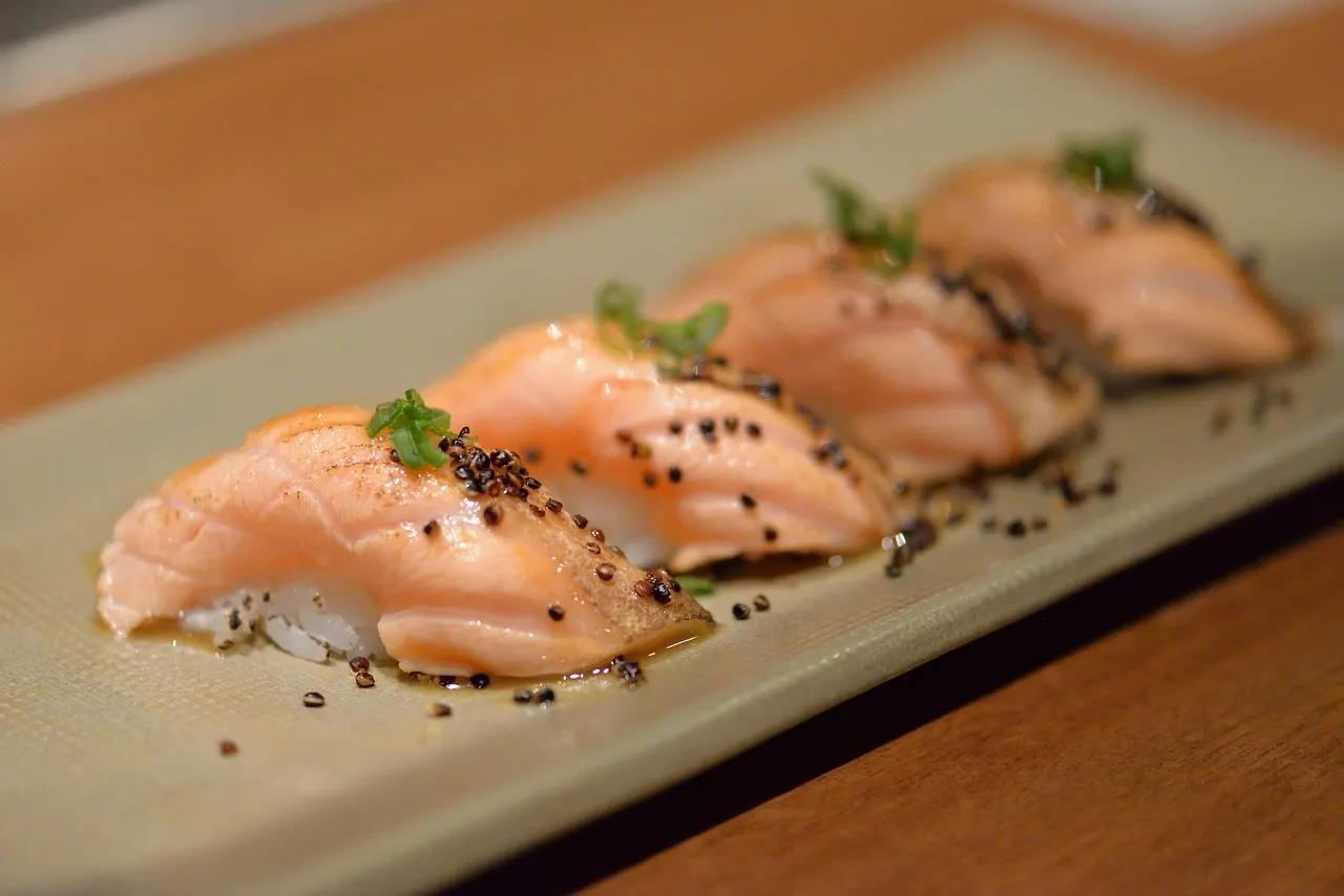 Vier stukjes gebrande zalmnigiri met zwarte sesam en kruiden op een langwerpig bord